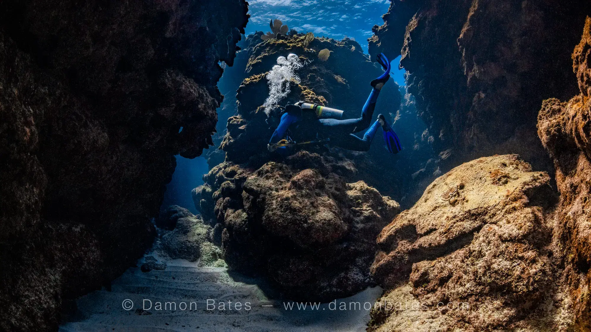 Scuba diver exploring a narrow coral canyon at Broadbelt Bommies, Ocean Frontiers, Grand Cayman — underwater photograph by Damon Bates
