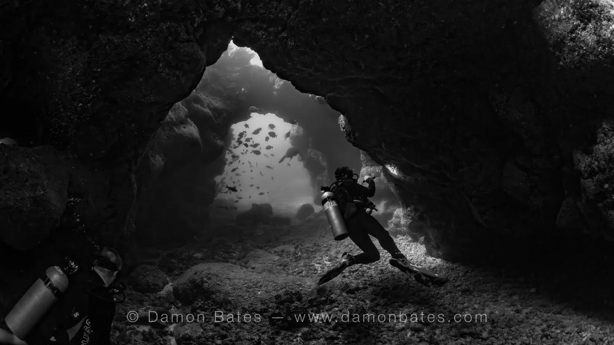 Scuba diver silhouetted in the opening of a lava cave at Sheraton Caverns, Kauai, Hawaii — black and white — underwater photograph by Damon Bates