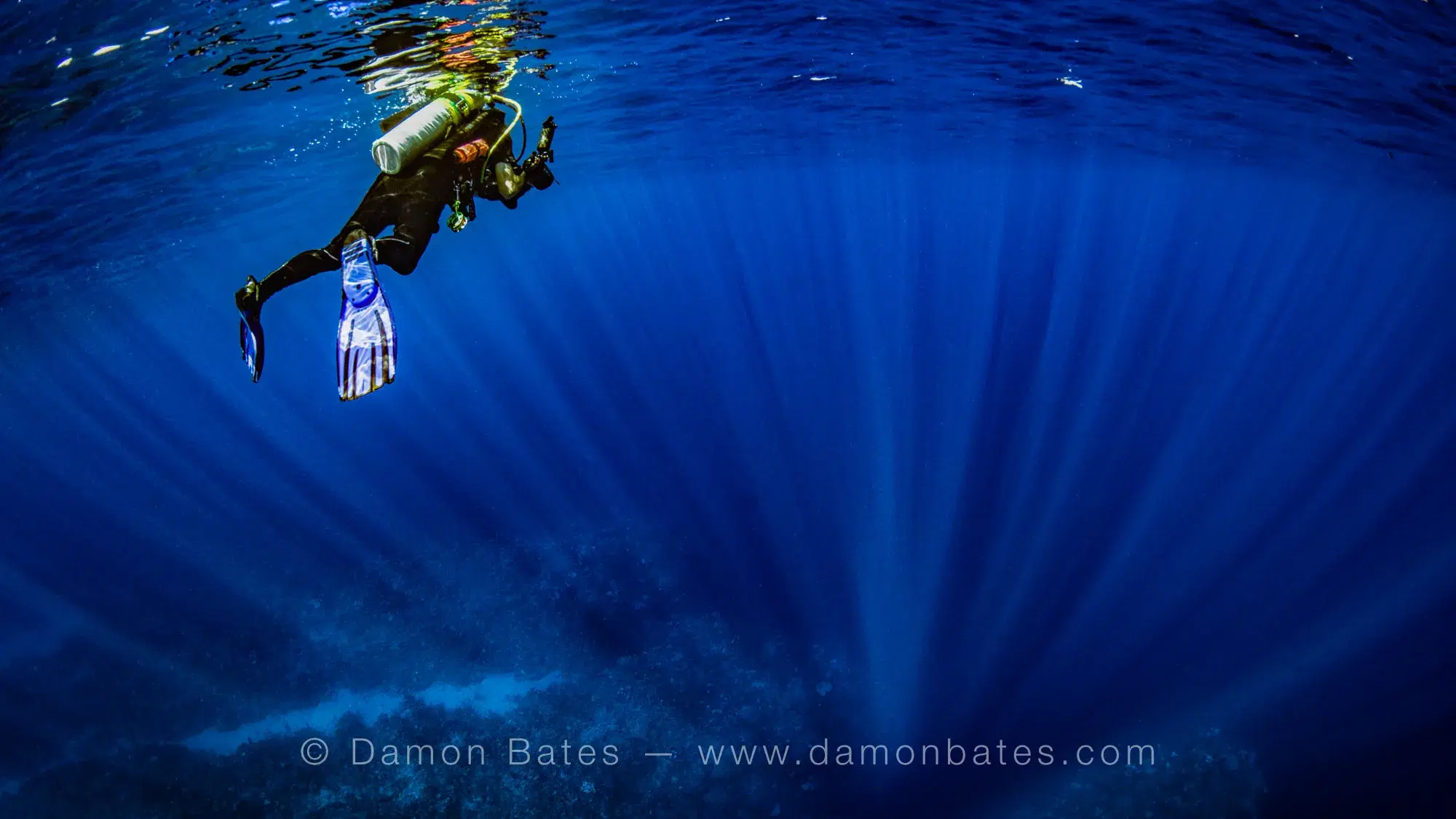 Scuba diver floating in blue water with sunrays fanning across the reef below, Ocean Frontiers, Grand Cayman — underwater photograph by Damon Bates