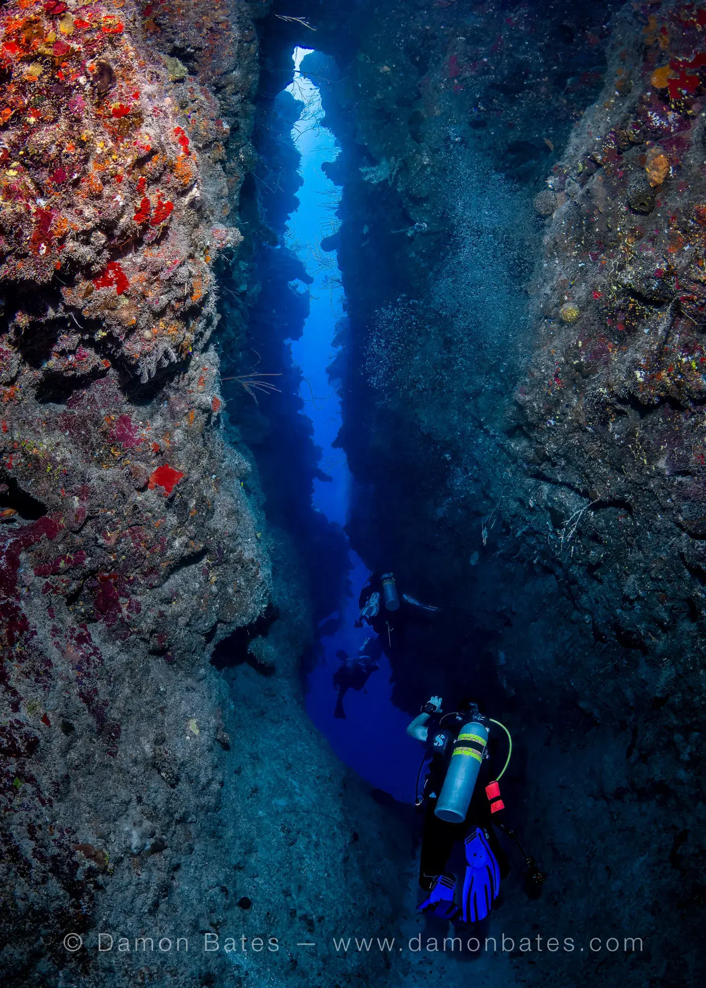 Scuba diver ascending through a narrow vertical crevice at Breakers Cutback, East End, Grand Cayman — underwater photograph by Damon Bates