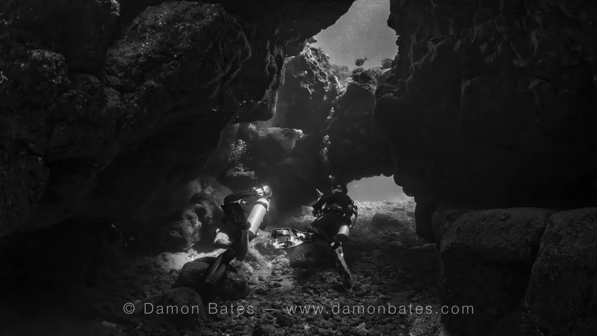 Two scuba divers exploring a lava cave at Sheraton Caverns, Kauai, Hawaii — black and white — underwater photograph by Damon Bates