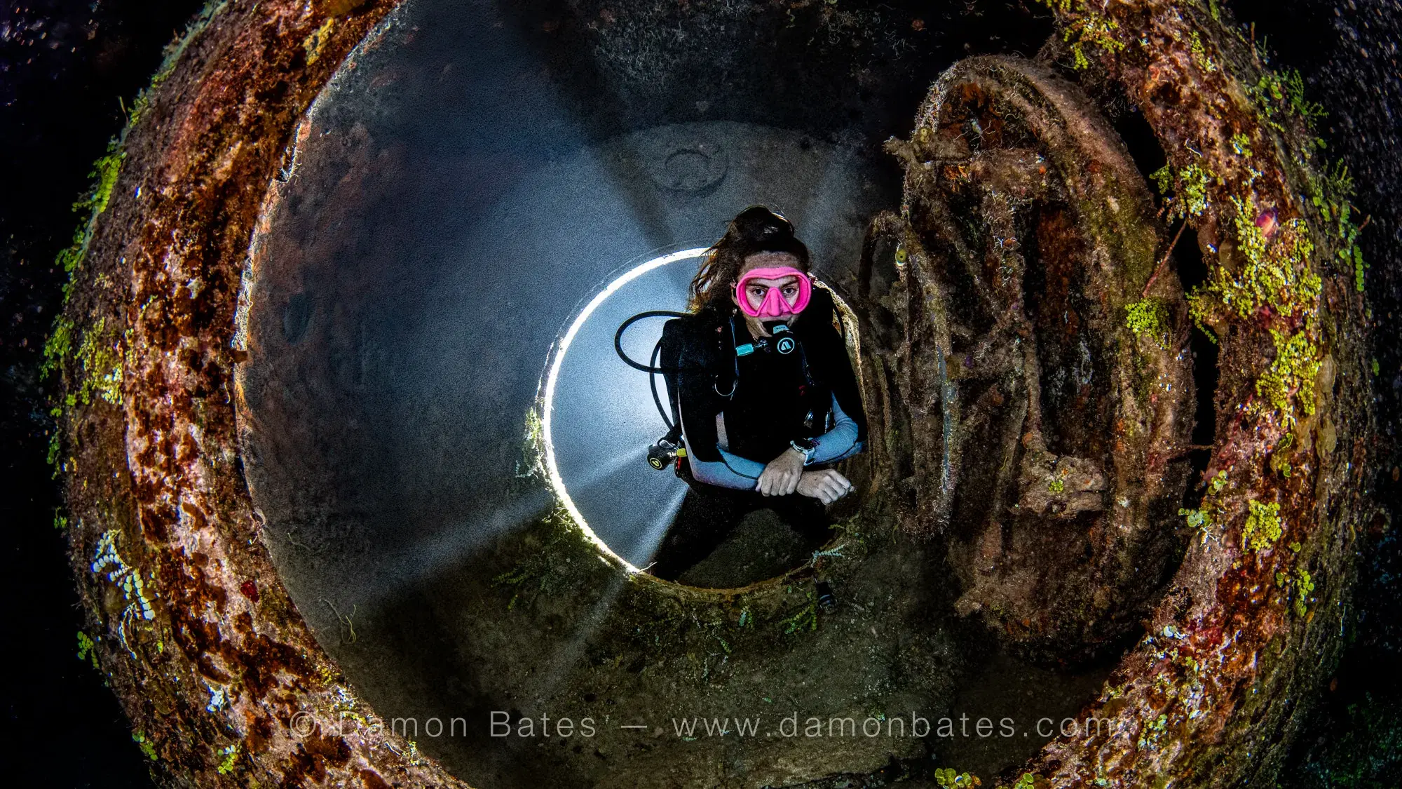 Scuba diver backlit in the decompression chamber hatch opening of the USS Kittiwake, Grand Cayman, 2025 — underwater photograph by Damon Bates