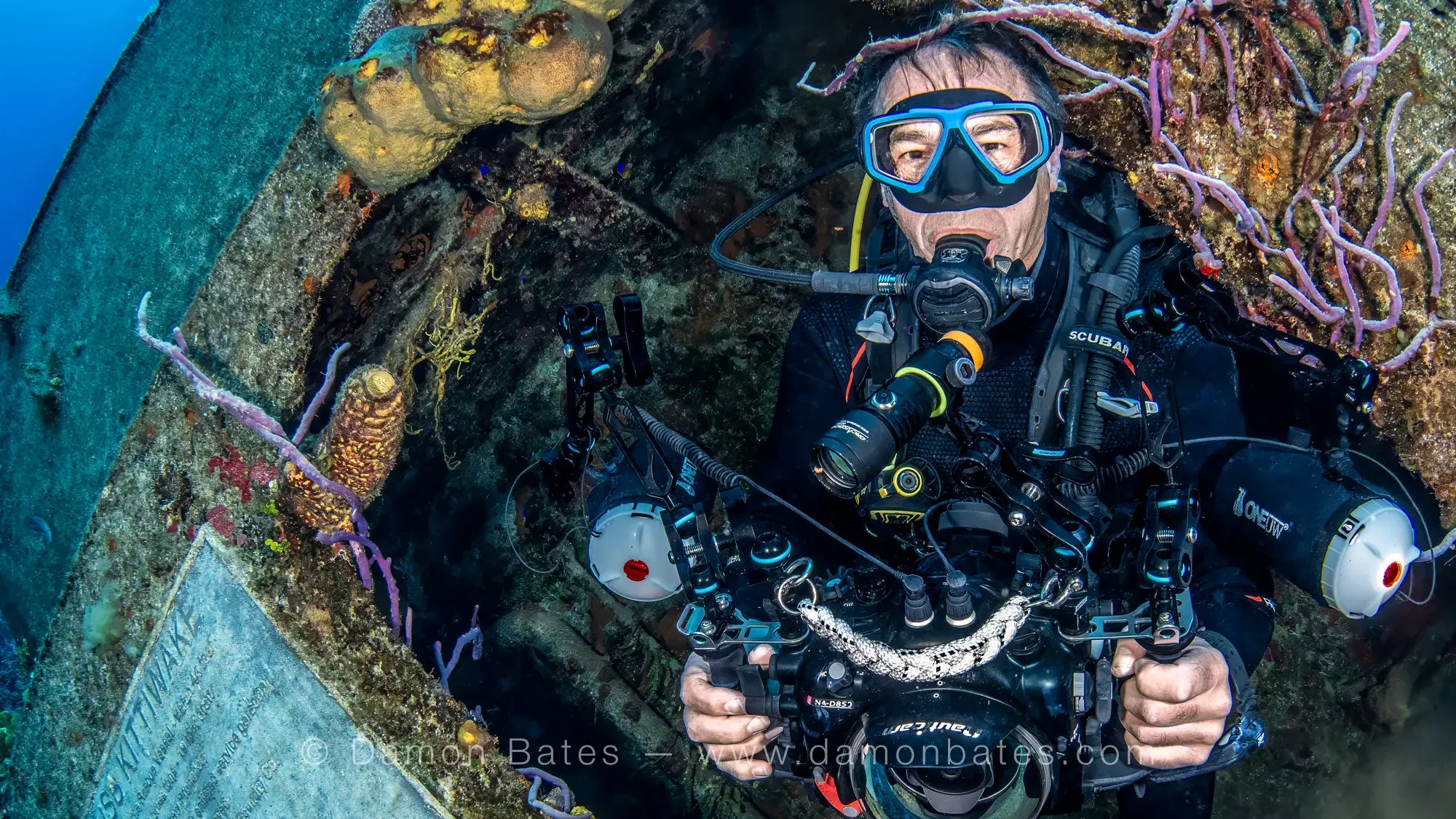Underwater photographer with full camera rig emerging from an opening in the USS Kittiwake, Grand Cayman, 2025 — underwater photograph by Damon Bates